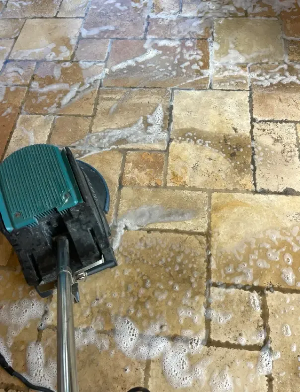 A hard-surface spinner tool cleaning a stone tile floor, foam lifting soil out of the grout lines